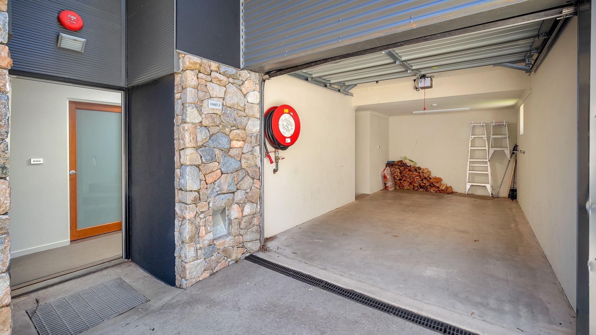A garage with a stone wall, a fire extinguisher, and a stack of firewood.