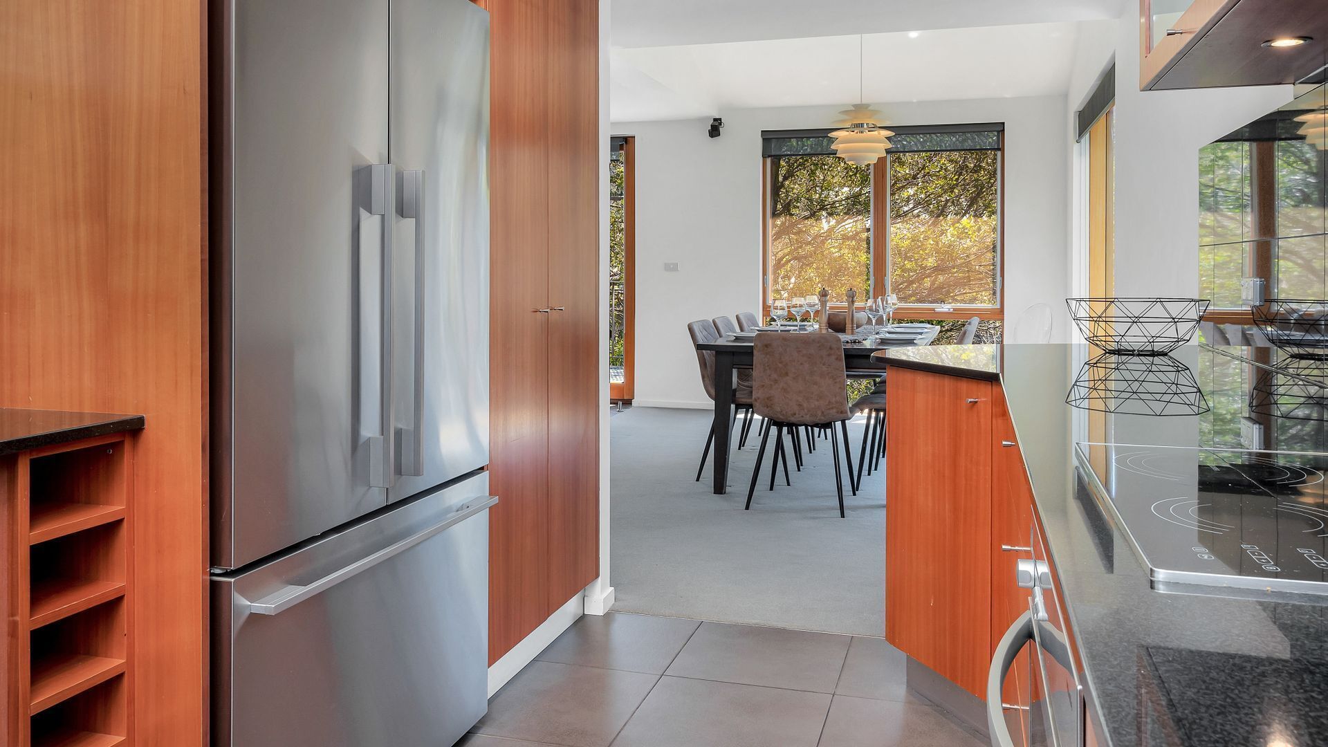 A modern kitchen with a stainless steel refrigerator, wooden cabinets, and a dining area with a table and chairs.