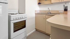 Pieni, käytännöllinen keittiö, jossa on valkoinen liesi, pesuallas ja beigenväriset kaapit.