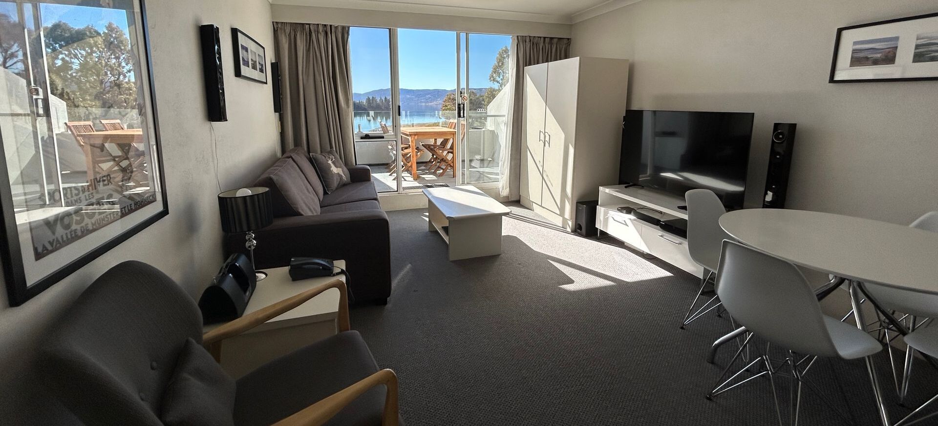 Une chambre d’hôtel moderne équipée d’un canapé, d’une table à manger, d’une télévision et offrant une vue sur un lac et des montagnes.