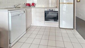 Une cuisine avec des meubles blancs, un lave-vaisselle, une cuisinière et un réfrigérateur.