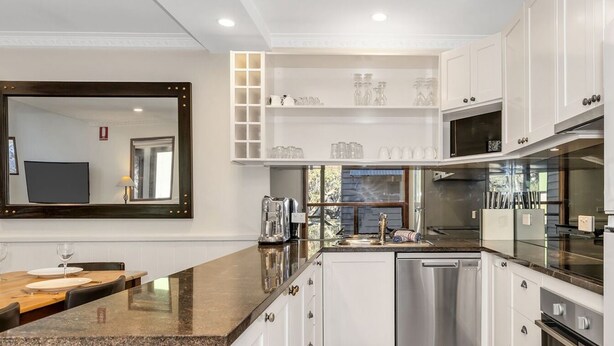 Una cocina moderna con gabinetes blancos, encimera de granito y electrodomésticos de acero inoxidable.