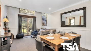 A dining area with a wooden table set for four, a sofa, and a large mirror on the wall.