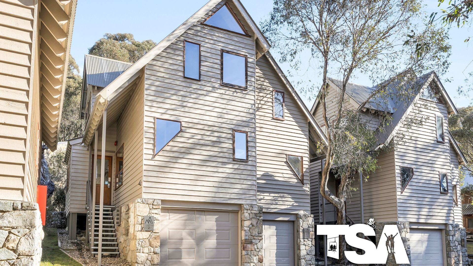 A two-story house with a garage, stone foundation, and a triangular window design.