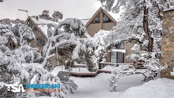A snow-covered lodge with multiple cabins, a stone wall, and snow-laden trees.