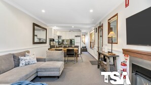 Una sala de estar moderna con un sofá, un comedor con una mesa y sillas, una cocina al fondo y una chimenea con un televisor encima.