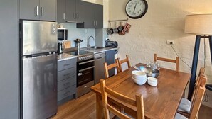 A compact kitchen with grey cabinets, a stainless steel refrigerator, a built-in oven, and a wooden dining table with chairs. - Alpine Mountain View 9 (Jindabyne)