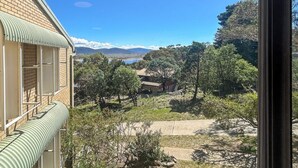 A view from a window overlooking a mountainous landscape with a building featuring a green awning and a brick facade. - Alpine Mountain View 9 (Jindabyne)