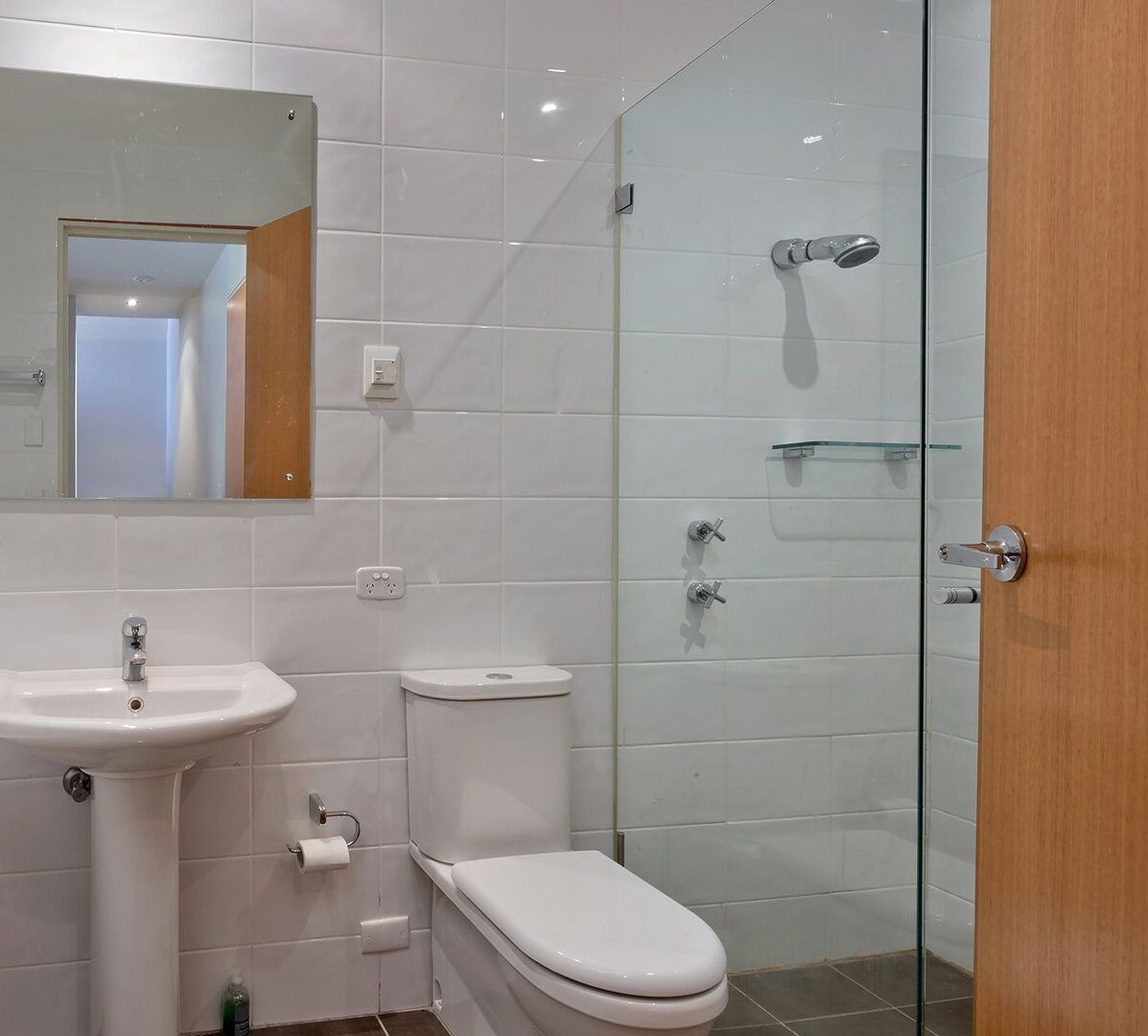 Un baño moderno con lavamanos, inodoro y cabina de ducha con mampara de vidrio.