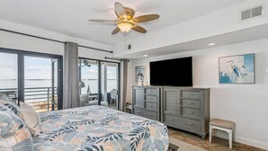 Ein Schlafzimmer mit Bett, Deckenventilator, Fernseher, Kommode und Fenster mit Blick.