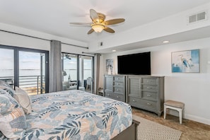 Ein Schlafzimmer mit Bett, Deckenventilator, Fernseher, Kommode und Fenster mit Blick.