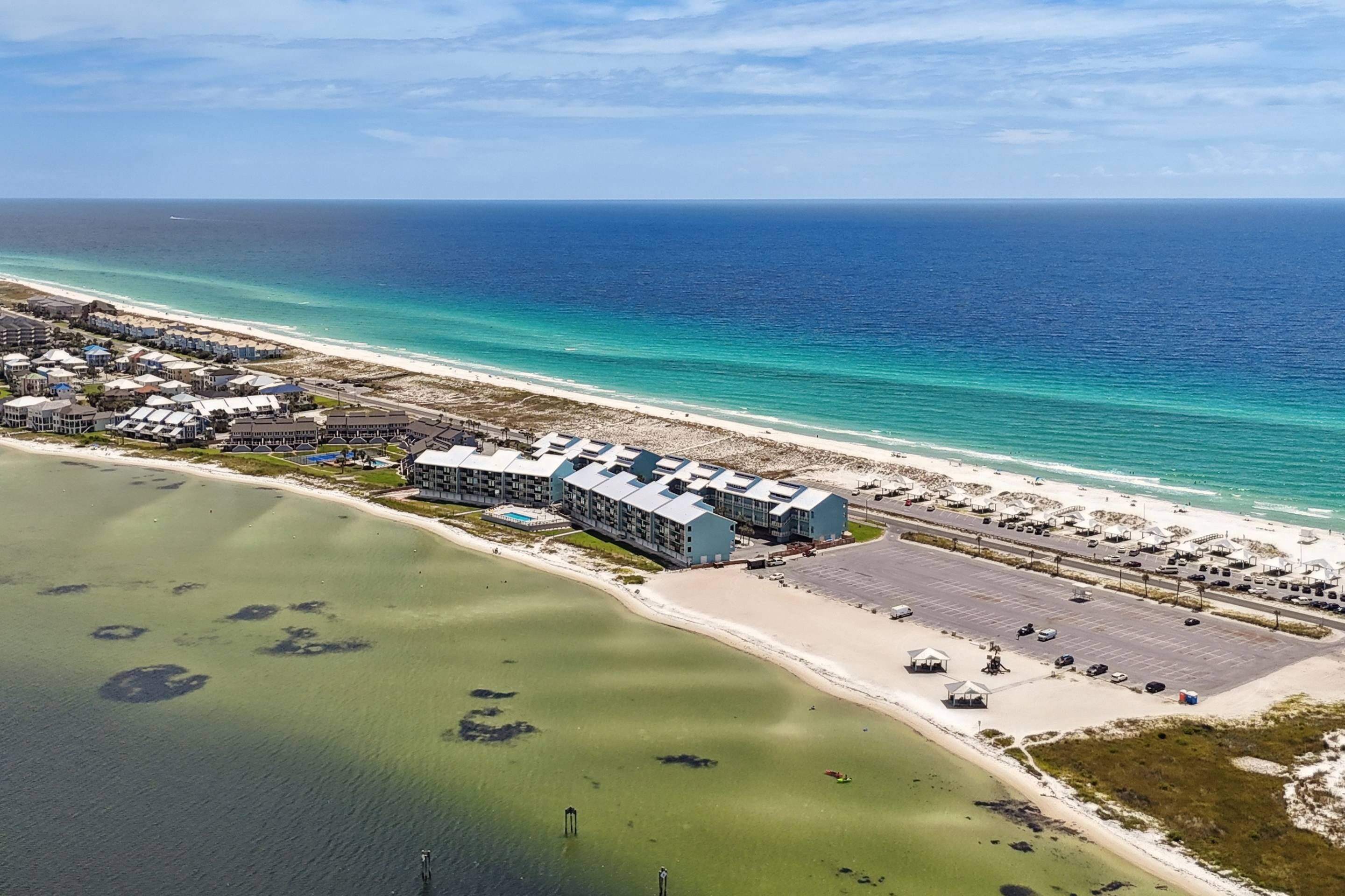An aerial view of a coastal hotel with multiple buildings, a parking lot, and a beach.