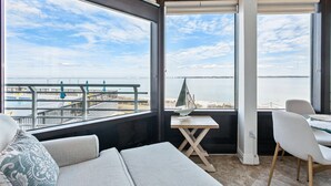 Ein Balkon mit Blick aufs Meer, ein kleiner Tisch mit einem Modellsegelschiff und eine Sitzecke mit Kissen.