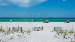 Ein Strand mit einer Holzlattenveranda, klarem türkisfarbenem Wasser und wolkenlosem Himmel.