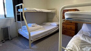 Une chambre avec un lit superposé, un radiateur, une commode en bois et une fenêtre.