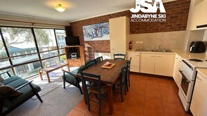 Une cuisine moderne avec des meubles blancs, une cuisinière et un évier. On y trouve un coin repas avec une table et des chaises en bois, ainsi qu’une grande fenêtre offrant une vue dégagée.