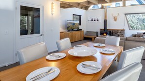 A dining area with a wooden table set for six, white chairs, and a stone fireplace in the background.