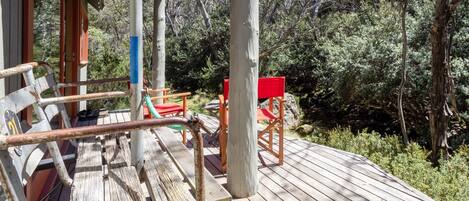 Une terrasse en bois avec des sièges extérieurs et une forêt luxuriante en arrière-plan.