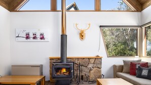 A cozy room with a stone fireplace, a wooden ceiling, and a large window offering a view of trees.