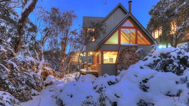 A modern house with a stone facade, large windows, and a wooden deck.