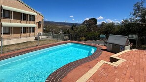 A rectangular swimming pool with a brick border, surrounded by a brick patio. - Alpine Mountain View 41 (Jindabyne)