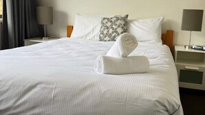 A hotel room with a neatly made bed, a bedside table with a lamp, and a chair. - Alpine Mountain View 41 (Jindabyne)