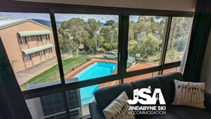 A room with a large window overlooking a swimming pool and a building. - Alpine Mountain View 47 (Jindabyne)