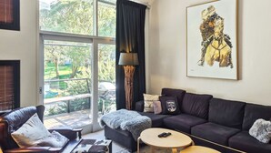 A modern living room with a dark sofa, a round coffee table, and a large window with a view of greenery.