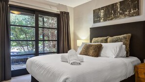 A hotel room with a large bed, a headboard with pillows, a window with curtains, and a painting on the wall.