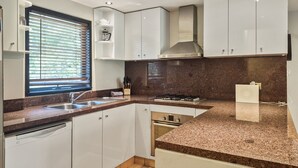 A modern kitchen with white cabinets, a granite countertop, a gas stove, and a built-in oven.