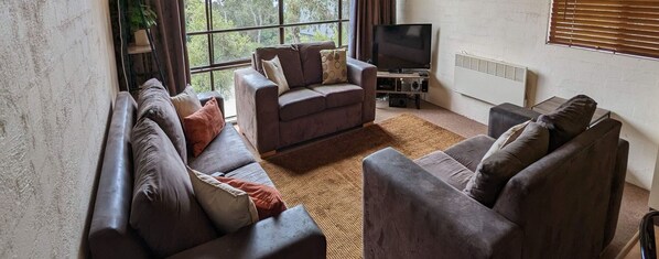 Relax in this stylish living room with a large window offering a view of the outdoors, a flat-screen TV, and a comfortable sofa and armchairs.