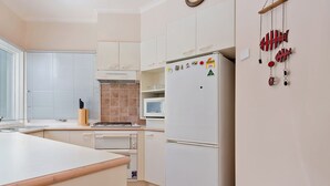 A modern kitchen with white cabinets, a built-in microwave, and a refrigerator. - Kaella - Central Village (Central Village)