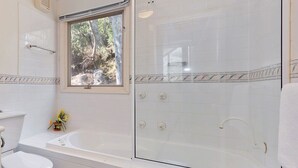 A bathroom with a bathtub, toilet, and a glass-enclosed shower area. - Kaella - Central Village (Central Village)