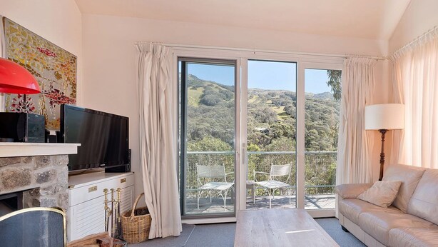 A living room with a sofa, a TV, a fireplace, and a balcony with chairs. - Kaella - Central Village (Central Village)