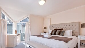 A bedroom with a large bed, a bedside table, a lamp, and a window with curtains. - Kaella - Central Village (Central Village)