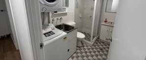Modern bathroom with washer and dryer, standard toilet, and glass-enclosed shower.