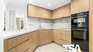 Una cocina moderna con armarios de madera, un lavamanos de acero inoxidable y un horno negro.