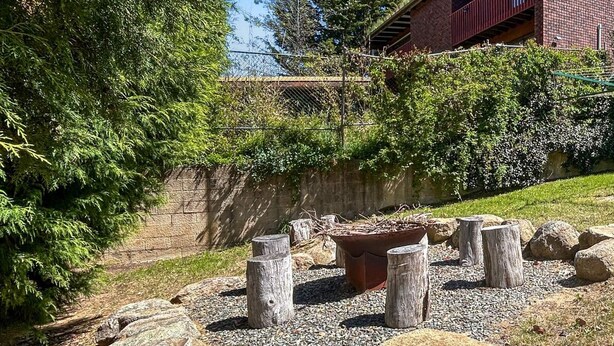 A garden area with large rocks, wooden stumps, and a brick building in the background.