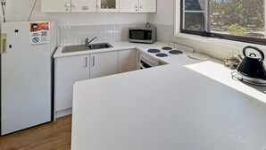 A compact kitchen with white cabinets, a microwave, a stove, and a kettle.