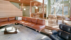 Ein modernes Wohnzimmer mit einer braunen Ledersofa, einem Glastisch und einem Essbereich mit Holzmöbeln.