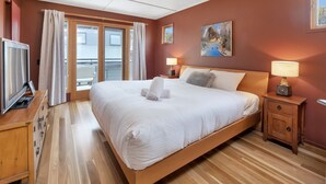 Ein Hotelzimmer mit einem großen Bett, einem Fernseher, einer Holzkommode und einem Balkon mit Vorhängen.