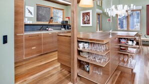 Eine moderne Küche mit Holzausstattung, einem integrierten Weinschränkchen und Blick ins Freie durch große Fenster.