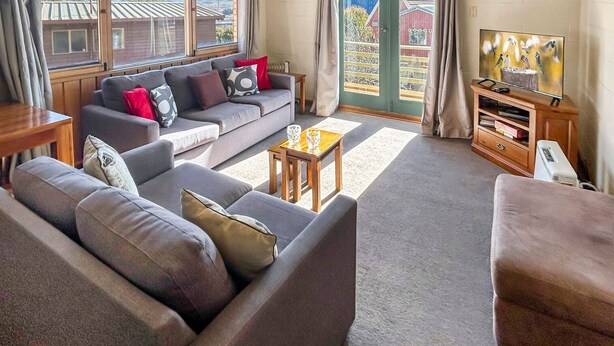 A living room with a sofa set, a coffee table, a TV, and a wooden cabinet. - Moonbah 2 two bedroom unit (Jindabyne)