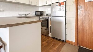 A kitchen with white cabinets, a microwave, a refrigerator, and a wooden door. - Moonbah 2 two bedroom unit (Jindabyne)