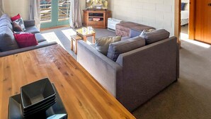 A cozy living area with a wooden table, grey sofas, and a television. - Moonbah 2 two bedroom unit (Jindabyne)