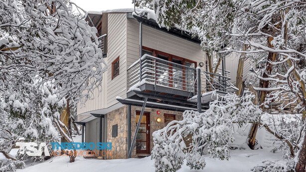 Ein zweistöckiges Gebäude mit einer Stein-Fassade, einem Balkon mit Metallgeländer und schneebedeckten Bäumen.