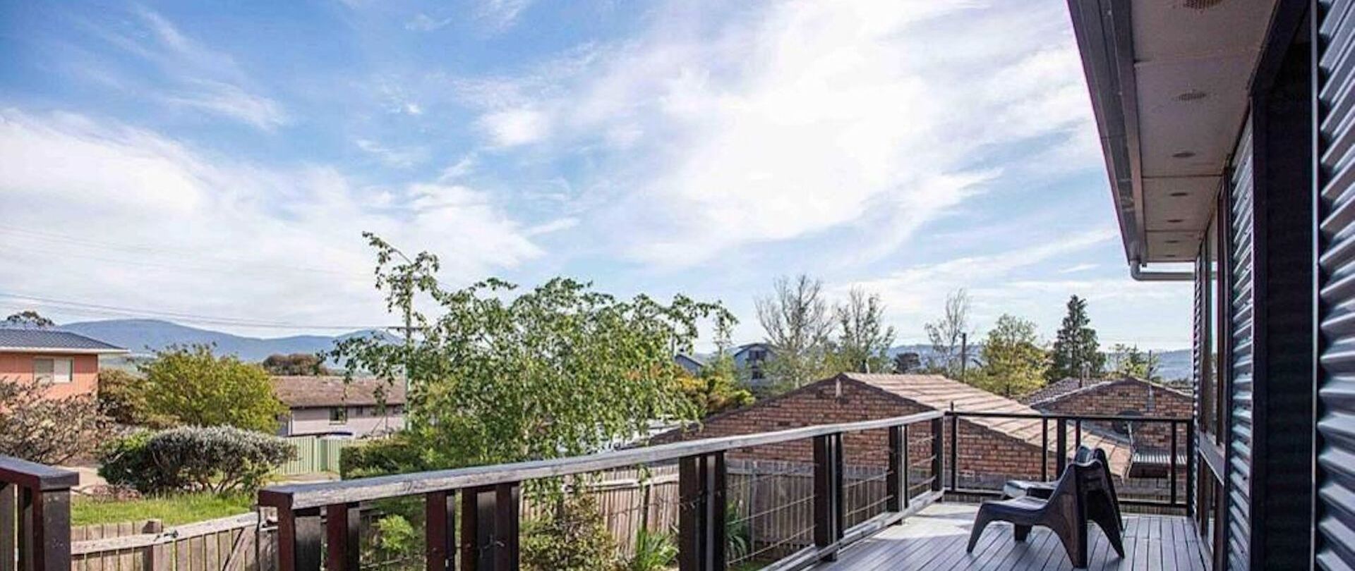 A balcony with a view of a residential area, a wooden deck, and a metal railing.