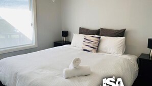 Una cama bien hecha con una toalla enrollada, dos mesitas de noche negras y una ventana con vistas.