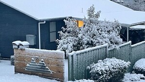 Una casa cubierta de nieve con un portón de madera, un garaje y un arbusto nevado.