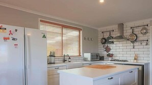 Una cocina moderna con armarios blancos, microondas integrado y un colgador de ollas sobre la estufa.